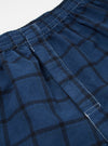 Close-up of Blue Check Boxer Short on a white surface. The fabric is a blue and black check pattern with an elastic waistband and white stitching.