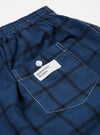 Close-up of the Blue Check Boxer Short on a white background. Features a blue and black check pattern, elastic waistband, and a pocket with a white label.