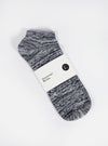 The Navy Slub Knit Ankle Slub Sock, packaged on a white surface. The sock is navy and white knit, with a paper label around it. 