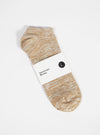 Studio shot of a Dark Sand Slub Knit Ankle Slub Sock on a white surface. The sock has a paper label around it.