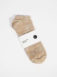 Studio shot of a Dark Sand Slub Knit Ankle Slub Sock on a white surface. The sock has a paper label around it.