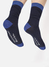Close-up of model wearing Navy Merino Classic Sock. Ribbed navy sock with blue toe and cuff. "Universal Works" in white on the foot. Studio shot on white background.