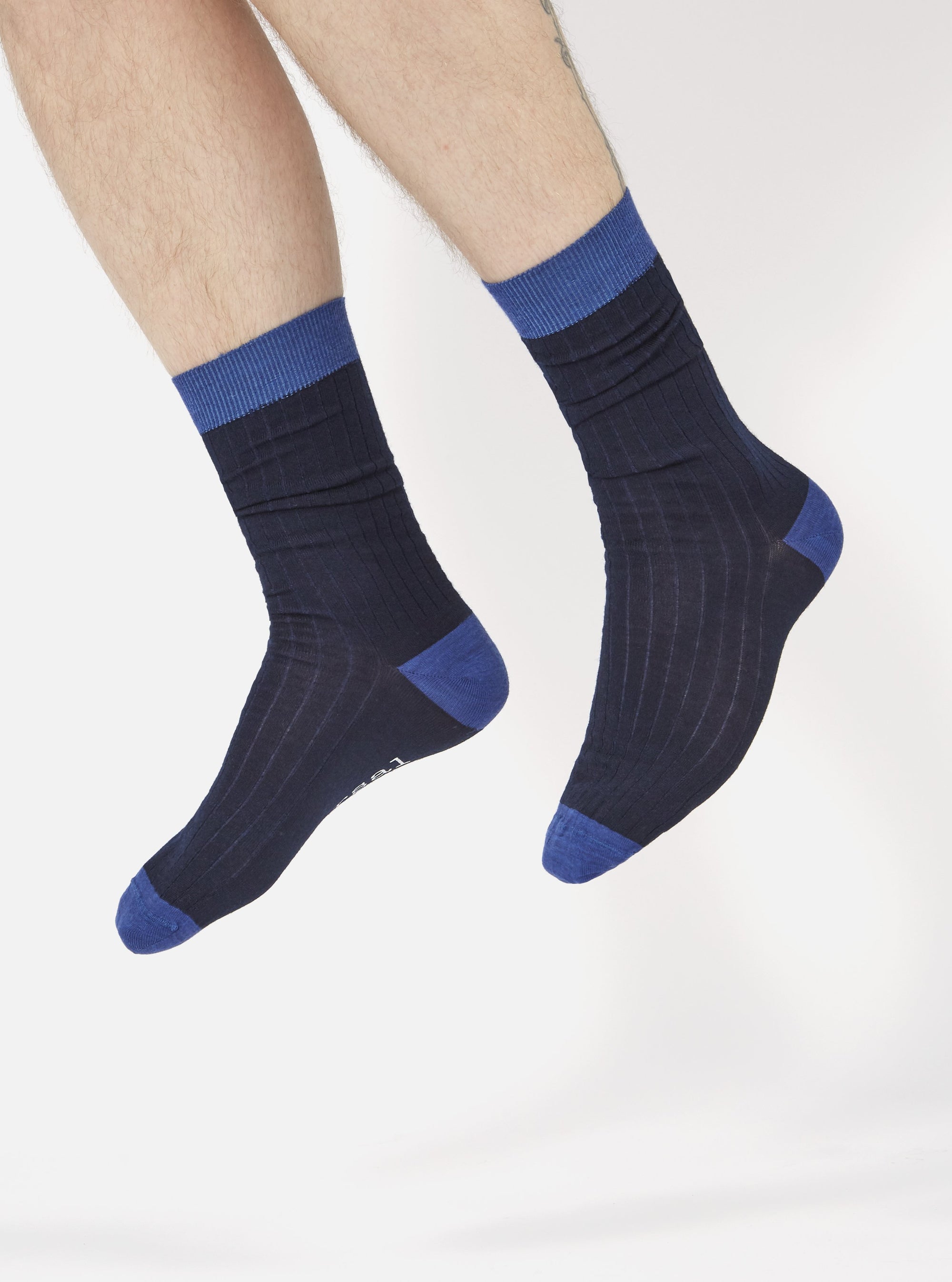A model wearing Navy Merino Classic Sock, a navy sock with a blue toe and cuff, on a white background.