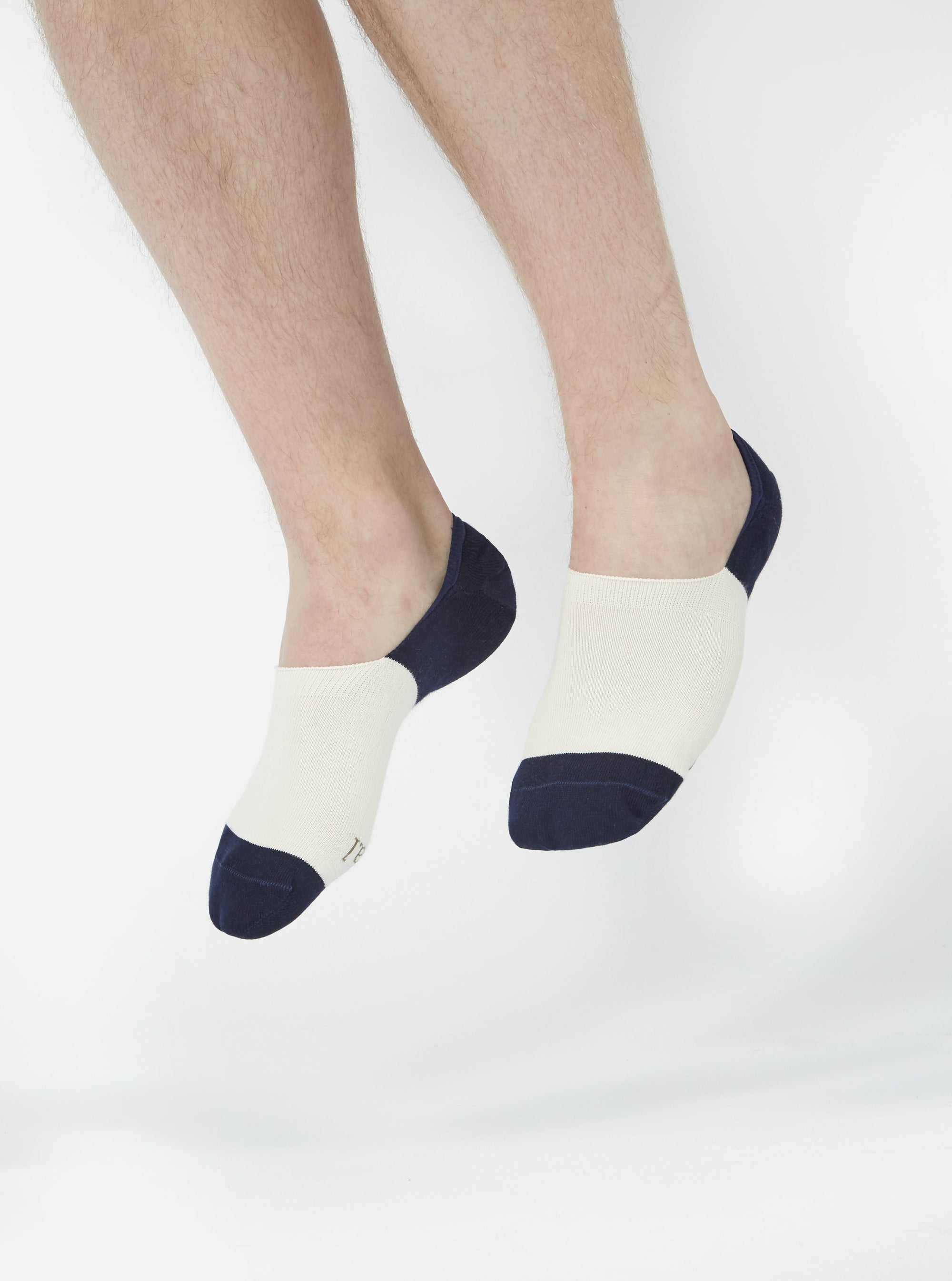 Close-up of a model's feet wearing Ecru/Navy Cotton Mix Knit No Show Socks. The socks are ecru with navy blue accents, set against a bright white background.