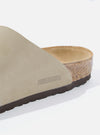 Close-up of a Birkenstock Zürich in taupe suede on a white surface. The brand name is subtly embossed on the side. The sole is visible, showing the cork layer.