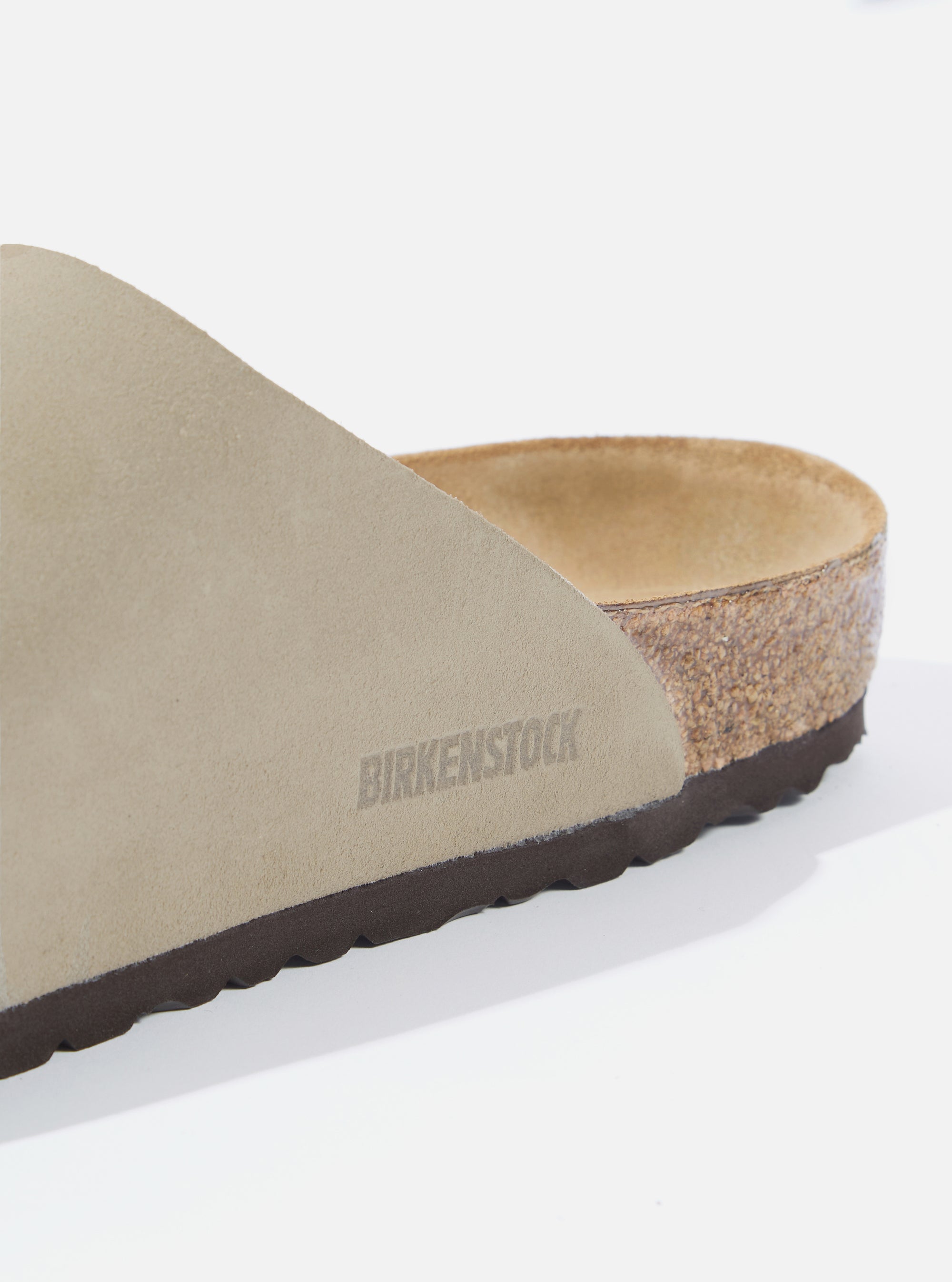 Close-up of a Birkenstock Zürich in taupe suede on a white surface. The brand name is subtly embossed on the side. The sole is visible, showing the cork layer.