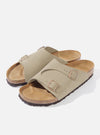 Studio shot of Birkenstock Taupe Suede Zürich sandals. The taupe suede contrasts with the cork footbed. The background is a clean, bright white.